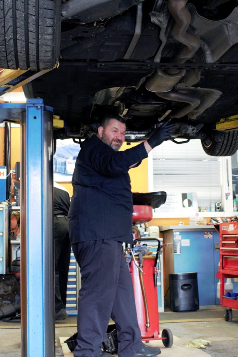 Technician working under a car on a lift at Bimmers Clinic