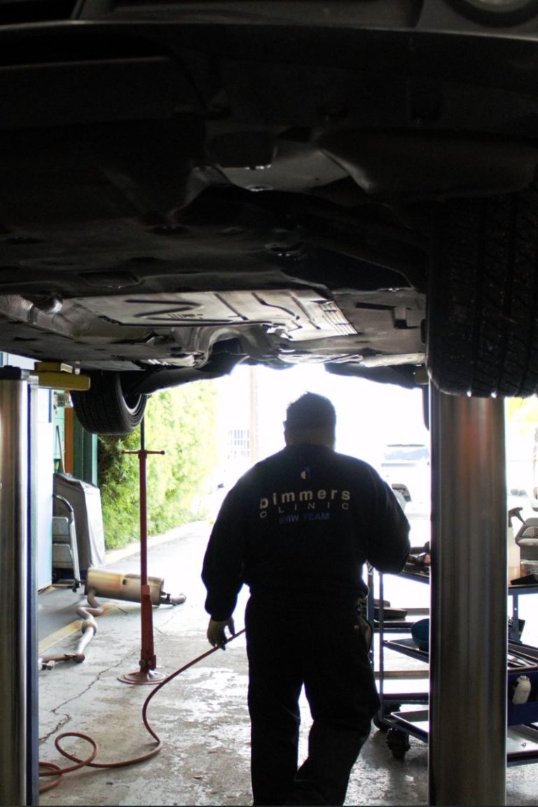 Technician in the Bimmers Clinic shop under a car on a lift